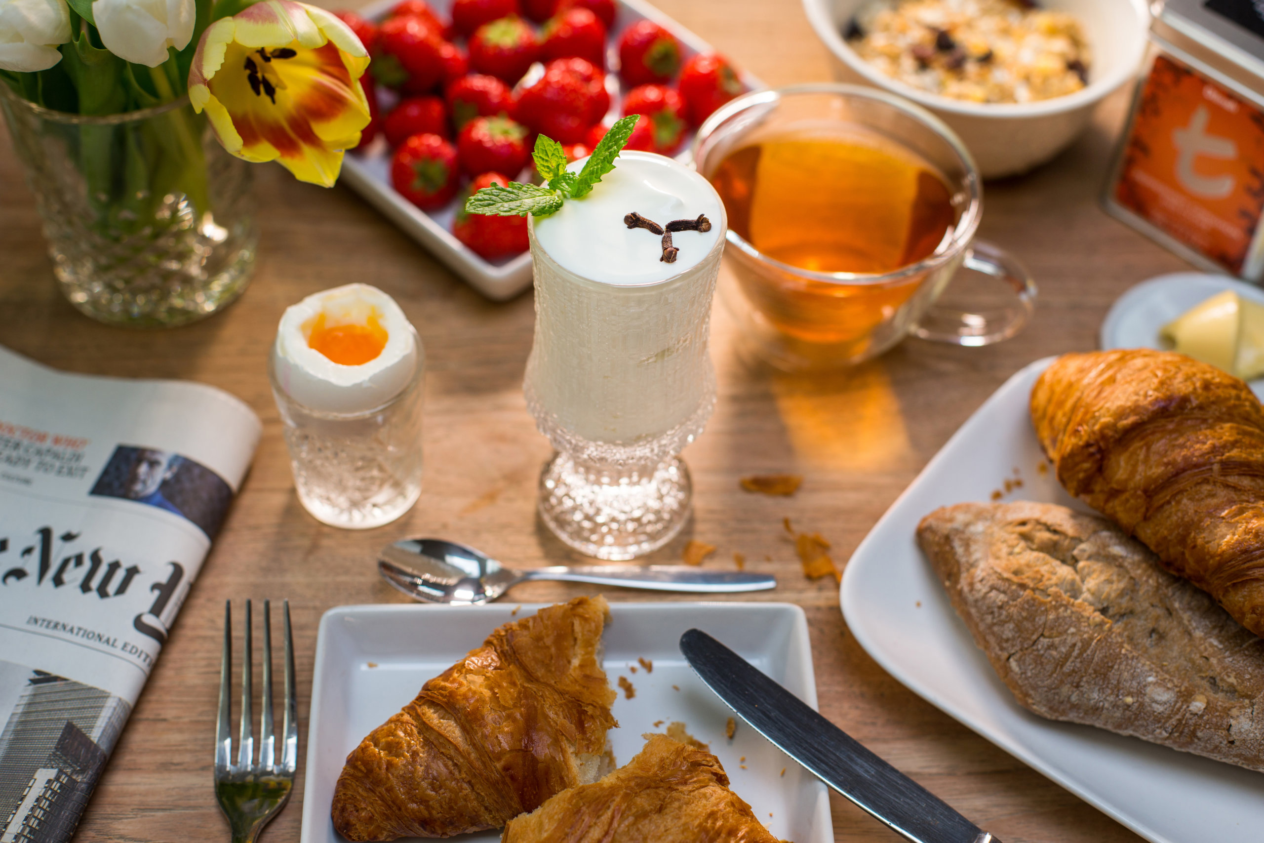 Tea inspired Breakfast with t-series tea croissants egg berries flowers and newspaper