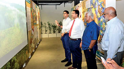 Dilhan and Malik looking at a presentation on white screen and explaining the Genesis Experience to two visitors
